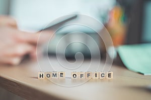 Home office concept: â€œHome Officeâ€ letters in foreground, man working in home office in blurry background