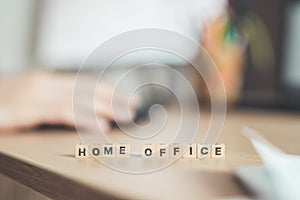 Home office concept: â€œHome Officeâ€ letters in foreground, man working in home office in blurry background