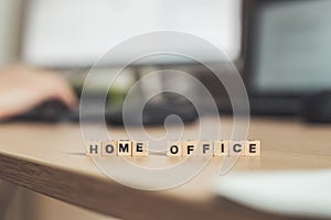 Home office concept: â€œHome Officeâ€ letters in foreground, man working in home office in blurry background