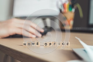 Home office concept: â€œHome Officeâ€ letters in foreground, man working in home office in blurry background