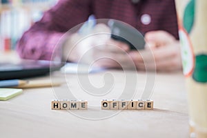 Home office concept: â€œHome Officeâ€ letters in foreground, man working in home office in blurry background