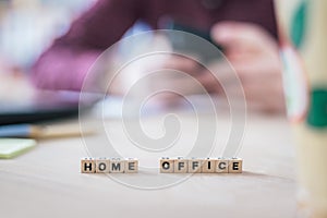 Home office concept: â€œHome Officeâ€ letters in foreground, man working in home office in blurry background