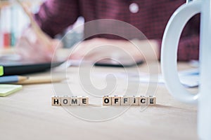 Home office concept: â€œHome Officeâ€ letters in foreground, man working in home office in blurry background