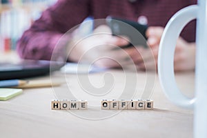 Home office concept: â€œHome Officeâ€ letters in foreground, man working in home office in blurry background