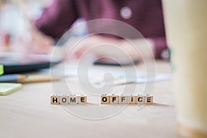 Home office concept: â€œHome Officeâ€ letters in foreground, man working in home office in blurry background