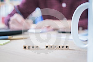 Home office concept: â€œHome Officeâ€ letters in foreground, man working in home office in blurry background