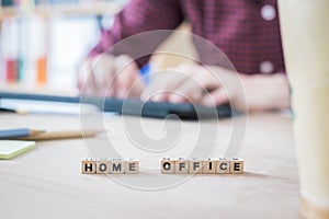 Home office concept: â€œHome Officeâ€ letters in foreground, man working in home office in blurry background
