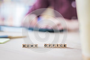 Home office concept: â€œHome Officeâ€ letters in foreground, man working in home office in blurry background