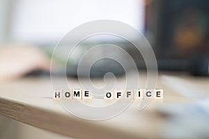 Home office concept: â€œHome Officeâ€ letters in foreground, man working in home office in blurry background