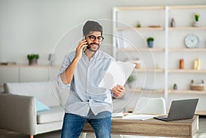 Home office. Confident arab entrepreneur talking with companion on phone and checking financial reports