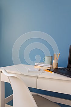 Home office of a creative entrepreneur with black laptop, empty white chair during lunch break. Modern creative workspace with cup