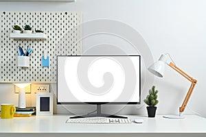 Home office desk with blank computer monitor, picture frame, lamp and peg board on wall