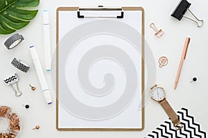 Home office desk with clip board mockup, glasses, golden stationery, green leaves and color markers for drawing