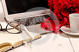 Home office desk with laptop, pink peonies, mug of coffee, stationery, glasses on a white background