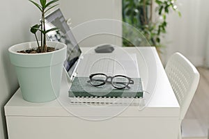 Home office desk table with laptop, notebook, phone, eyeglasses, home plant