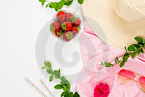 Home office desk workspace with straw hat, pink cloth, strawberries, branch of barberry, sunglasses on white background. Flat lay