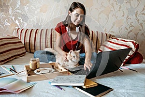 Home office, work space, work from home concept. Young woman with laptop and cat working at sofa. Flexible work hours