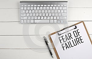 Home office workspace with keyboard, clipboard and pen with text FEAR OF FAILURE on white wooden background ,business concept