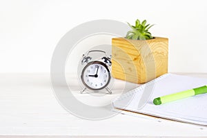 Home office workspace mockup with notebook, pen, alarm clock, plant in wooden potted and accessories on white wood desk background