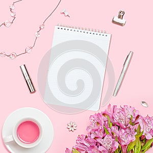 Home office workspace. Notebook with copyspace. Woman fashion accessories and flowers on pink background.