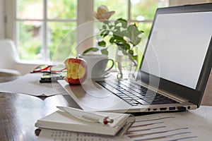 Home office workspace for a small business, on the desk a laptop with empty screen, papers, coffee cup, glasses and a bitten apple