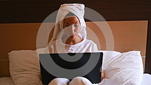 Home office. Young woman sitting on bed, working on laptop.