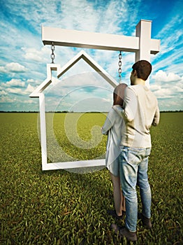 Home ownership dream. A couple standing before a real estate home sign with a grass field and beautiful sky background.