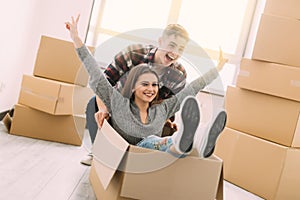 Home, people, moving and real estate concept - happy couple having fun and riding in cardboard boxes at new home