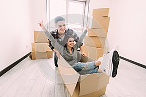 Home, people, moving and real estate concept - happy couple having fun and riding in cardboard boxes at new home