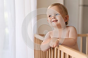 Home portrait of cute little baby boy in bed with pensive face looking at copy space