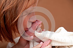 Home portrait of mother, hands holding and kissing her child, sweet newborn baby pink cute feet. Concept of the long