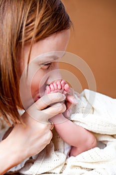 Home portrait of mother, hands holding and kissing her child, sweet newborn baby pink cute feet. Concept of the long