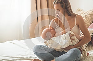 Home portrait of a newborn baby with mother on the bed. Mom holding and kissing her child.