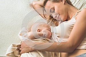 Home portrait of a newborn baby with mother on the bed. Mom holding and kissing her child.