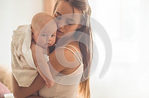 Home portrait of a newborn baby with mother on the bed. Mom holding and kissing her child.