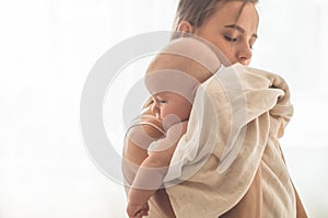 Home portrait of a newborn baby with mother on the bed. Mom holding and kissing her child.