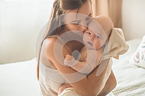 Home portrait of a newborn baby with mother on the bed. Mom holding and kissing her child.