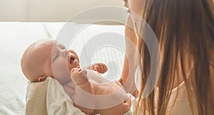 Home portrait of a newborn baby with mother on the bed. Mom holding and kissing her child.
