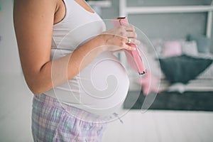 Home portrait of young pregnant woman preparing for childbirth and doing everyday homework at nursery.