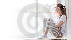 Home quarantine banner. A Caucasian woman on sick leave is sitting at the window in a medical protective mask, looking sadly at