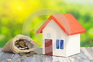 A home with red roof on green background with bag from sack with coins money inside concept of sell or buy home