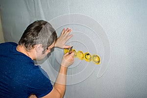 Home redecoration, young man pasted wallpaper and cuts places of the sockets. Wallpapering in apartment.