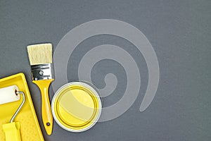 Home renovation and repair concept. paintbrush, sponge roller and can of yellow paint on gray background