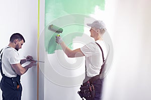 Home renovation worker with a tool belt painting a wall green wi