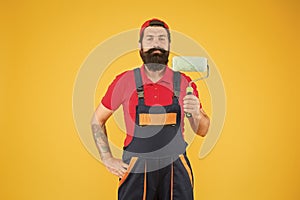 Home repair worker. bearded man worker with roller tool. hipster builder in cap yellow background. erector assistant in