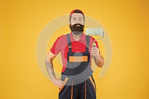 Home repair worker. bearded man worker with roller tool. hipster builder in cap yellow background. erector assistant in photo