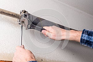 Home repairman uses tools to work on a garage door spring