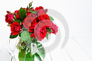 Home roses in a glass vase on a white wooden table. With copy space