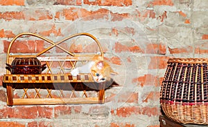 Home rustic interior. Brick wall with a wooden shelf and a clay pot, a ginger kitten and a wicker basket