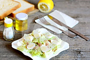 Home salad with napa cabbage, quail eggs and canned tuna fish. Tasty salad on a plate, fork, knife, olive oil bottle, salt shaker